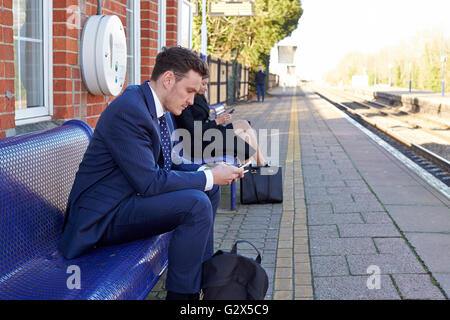 Commuters Waiting On Railway Platform Using Mobile Phones Stock Photo