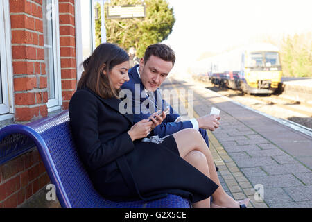 Commuters Waiting On Railway Platform Using Mobile Phones Stock Photo