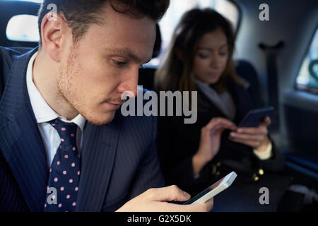 Businesspeople Travelling In Taxi Using Mobile Phones Stock Photo