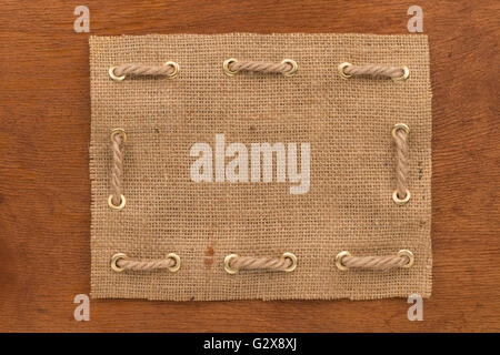 Frame made of burlap with a rope threaded through in gold rings, lie on a wooden surface, as background Stock Photo