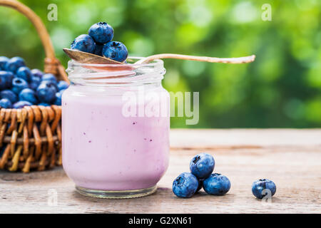 Blueberries yogurt in jar, basket of berries and saucer with bilberries on table outdoors. Stock Photo