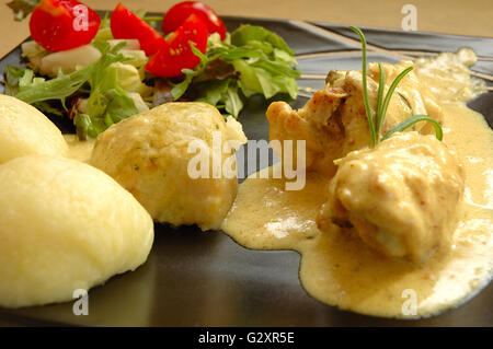 Dish consisting of rabbit meat, dumplings and salad served on black plate Stock Photo