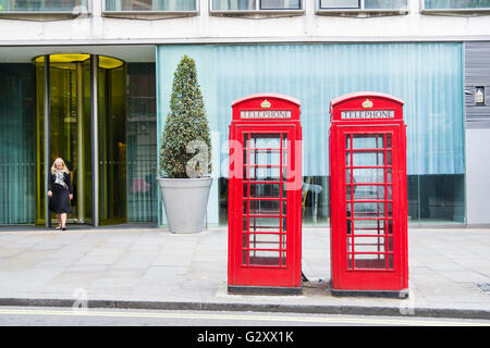 A woman emerges from an office door behind two Grade II listed Sir Giles Gilbert Scott K6 London telephone kiosks, London, England, U.K. Stock Photo