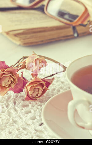 Dry rose on knitted napkin, old book and glasses in vintage style (toning) Stock Photo