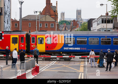 People / pedestrians / person wait / waits / waiting at a railway level crossing barrier as train passes through the crossing. Stock Photo