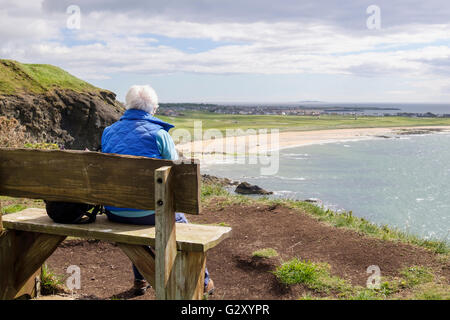 Retired senior woman retiree resting on a bench seat by Fife Coastal Path looking to West Bay in Firth of Forth. Elie and Earlsferry Fife Scotland UK Stock Photo