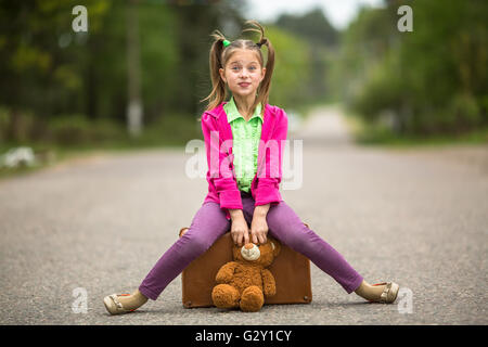 Little girl traveller in bright clothes on the road with a suitcase and a Teddy bear. Stock Photo