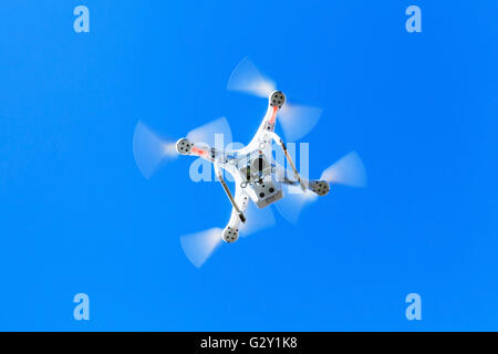 White quadrocopter in blue sky, drone controlled by wireless remote Stock Photo