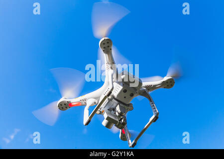 White quadrocopter flying in blue sky, drone controlled by wireless remote Stock Photo