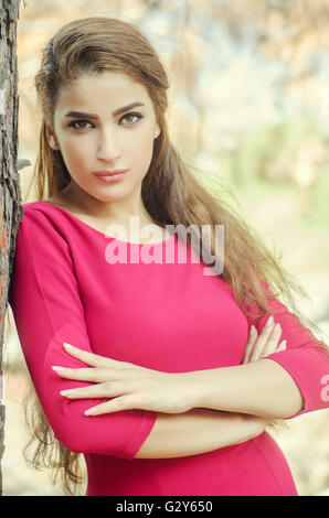 Beautiful young woman arms folded leaning against a tree Stock Photo