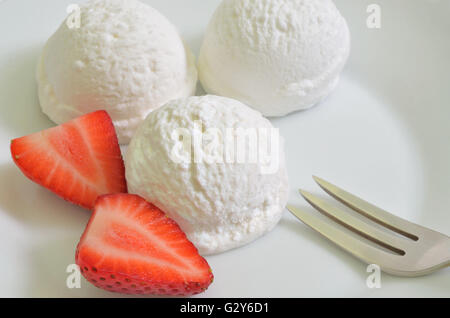 three  scoops of white ice cream, vanilla, lemon, coconut, yogurt or buttermilk flavor, with strawberries on white plate Stock Photo