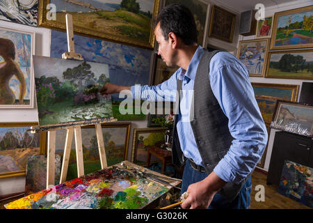 Artist working in a gallery or studio selecting a particular hue from a colorful palette of blended oil paints as he works on a Stock Photo