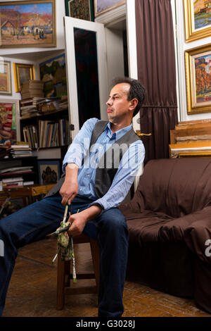Male handsome artist  sitting painting in a studio or gallery holding  paintbrushes and a rag Stock Photo