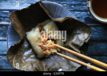 Lo Mai Gai. Steamed parcel of sticky rice with pork, shrimp, and egg in lotus leaf with a chunk being picked-up Stock Photo