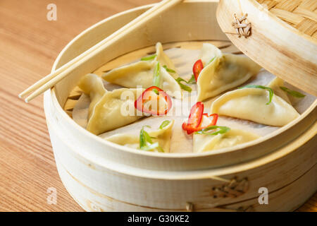 Dim sums - wontons -with a chicken meat  in a bamboo box on wooden table in asian restaurant Stock Photo