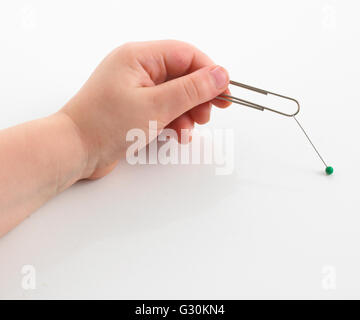 Child holding paper clip beside push pin, close-up Stock Photo
