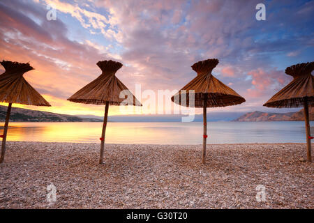 Straw umbrellas on the beach in Baska on island Krk Stock Photo