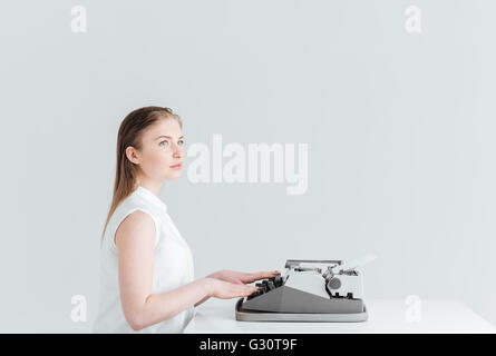 Pensive woman typing on retro machine isolated on a white backgound Stock Photo