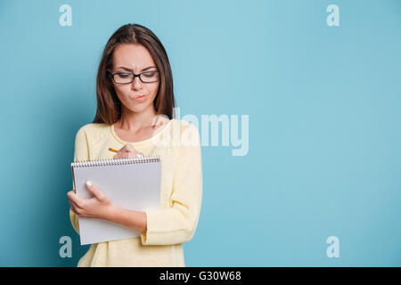 Serious pensive young girl making notes in the notebook isolated on the blue background Stock Photo