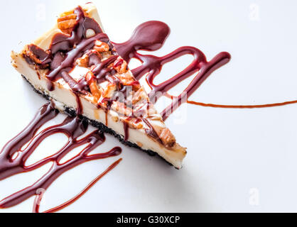 Homemade Turtle Cheesecake. Slice of turtle cheesecake garnished with chocolate on a white background. Stock Photo