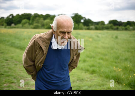 An elderly man with dementia looking thoughtful, walking on his own in the countryside looking confused and vulnerable. Stock Photo