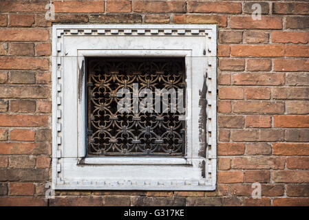 Square small window with white frame and decorative metallic grid on a brick wall in Venice Stock Photo