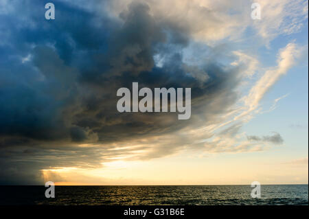 Storm clouds is an ominous storm moving in over the ocean as a bright set of sunrays burst through the darkness to light the way Stock Photo