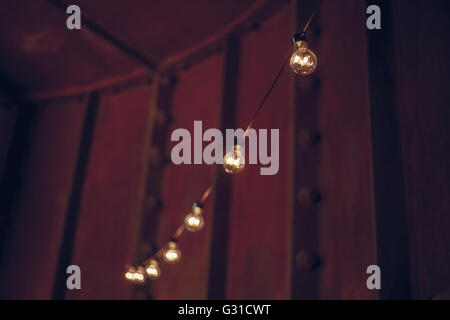 String wired bulbs hanging inside dark room, festive illumination, holiday concept Stock Photo