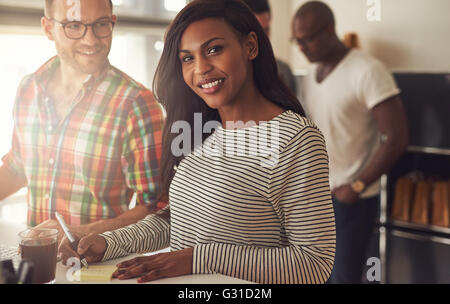Cute single African American woman in striped shirt writing notes on desk next to man at work Stock Photo