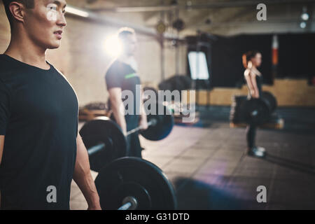 Fit young man lifting barbells looking focused, working out in a gym with other people Stock Photo