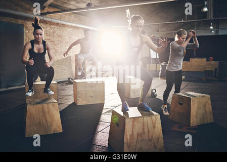 Fit young people doing box jumps as a group in a gym Stock Photo