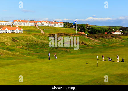 Golfers playing on the fifth green of the Ailsa Golf course of Trump Turnberry with the hotel and clubhouse in the background Stock Photo