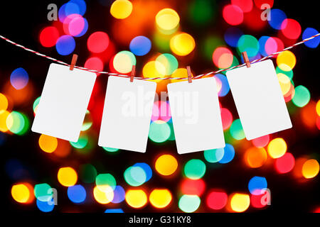 Blank paper or photo frames hanging on the red striped rope. Blurred defocused multi color lights background, Template for your design. Stock Photo