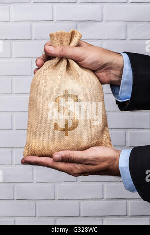 Hands holding a sack of money and white brick background Stock Photo