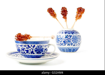 Blue pattern painted vintage cup of tea with brown sugar stirrer on top isolated on white. Stock Photo