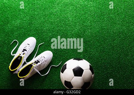 Soccer ball and cleats against green artificial turf, studio sho Stock Photo