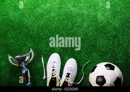 Soccer ball, cleats and trophy against green artificial turf Stock Photo