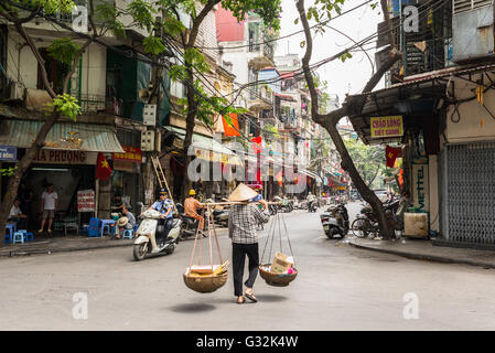 Street vendor transporting goods in baskets using a carrying pole in Hanoi's Old Quarter. Stock Photo