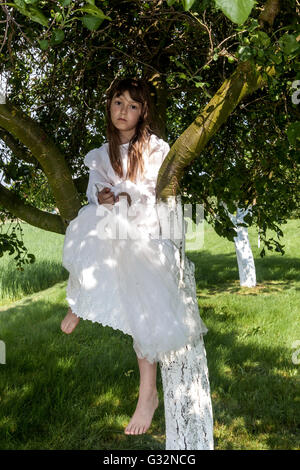 6- 7 year old girl in white dress sitting in a treetop, girls games Bride Stock Photo