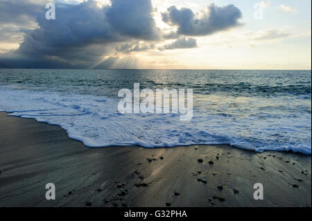 Ocean sunset sun rays is an ominous storm moving in over the ocean as a bright set of sunrays burst through the darkness to ligh Stock Photo