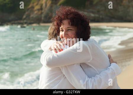 Two women standing on beach hugging Stock Photo