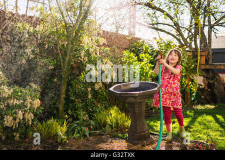 Girl watering plants in garden with hosepipe Stock Photo