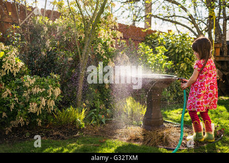 Girl watering plants in garden with hosepipe Stock Photo