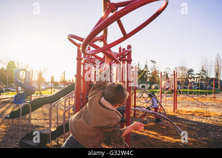 Rear view of boy swinging on monkey bars in playground Stock Photo