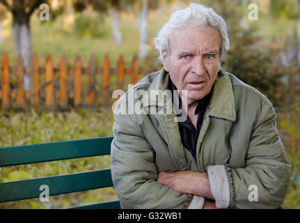 Portrait of Senior Man sitting on bench in garden with arms crossed Stock Photo