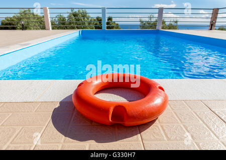 Orange life buoy lying at blue swimming pool in Greece Stock Photo