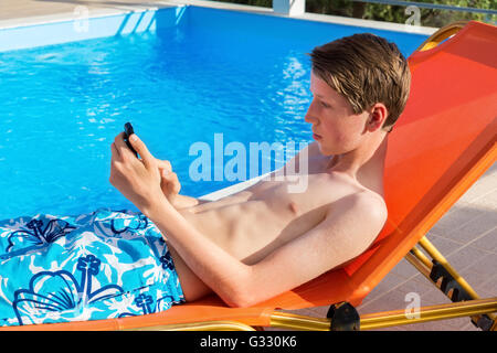 Young caucasian man lying on sunlounger  operating mobile phone at swimming pool Stock Photo