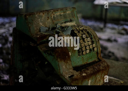 An old rusty cash register on the floor of an abandoned store in the ghost town of Pripyat which was evacuated in 3 hours shortly after Chernobyl nuclear plant accident in Ukraine. 04 June 2016. The Chernobyl accident occurred on 26 April 1986 at the Chernobyl Nuclear Power Plant in the city of Pripyat and was the worst nuclear power plant accident in history in terms of cost and casualties. Stock Photo