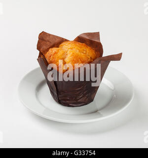 Delicious muffin cake in brown paper on the plate on white background. Stock Photo