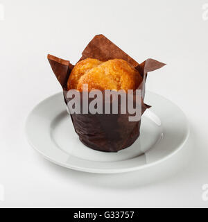 Delicious muffin cake in brown paper on the plate on white background. Close up side view. Stock Photo